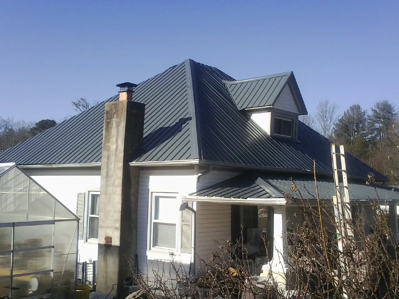 Dark blue standing seam metal roof on a white farmhouse with dormer — Slate & Tile Roof Repair by Roofing Brothers in Hughson