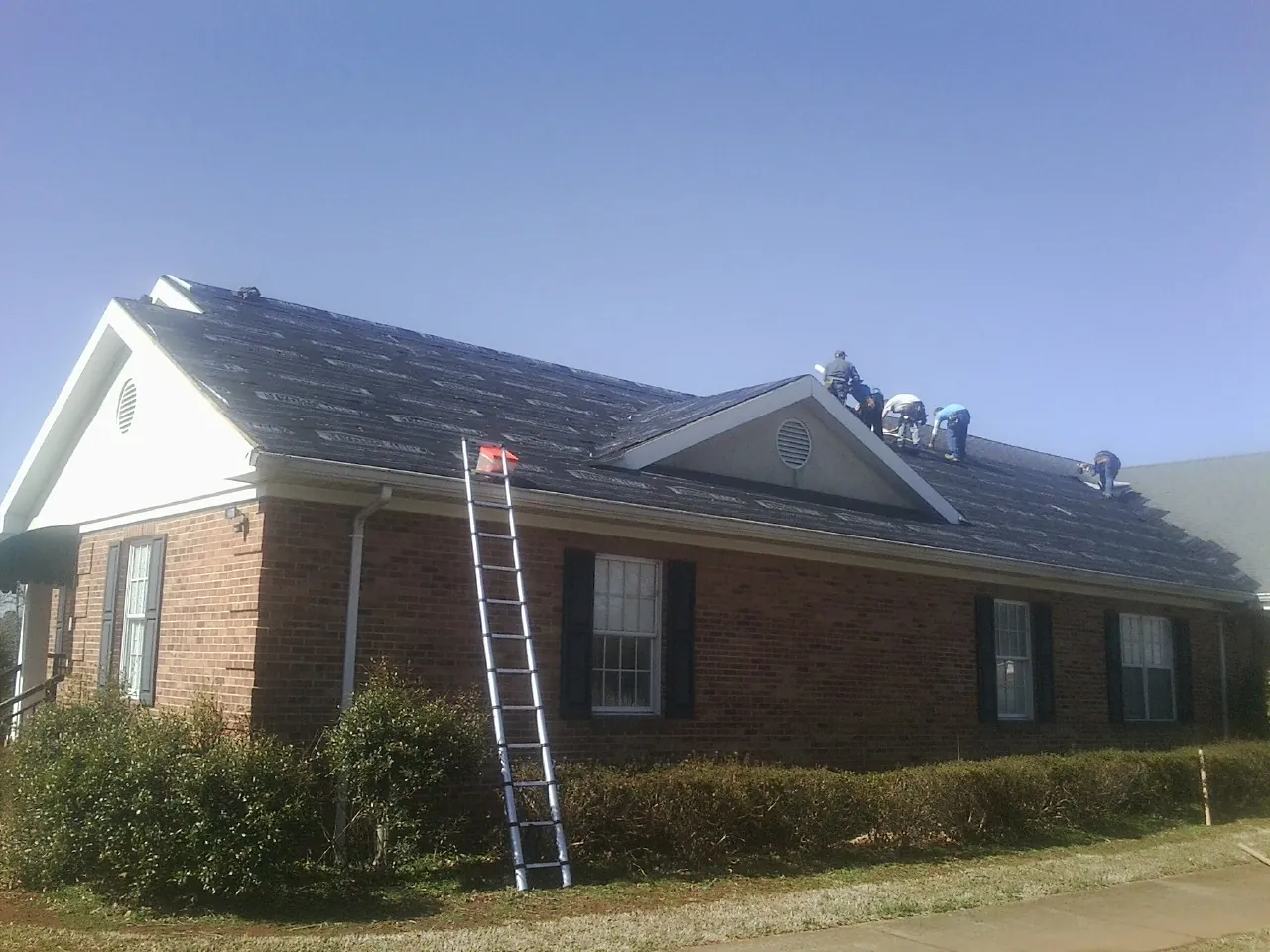 Crew tearing shingles off a brick ranch roof with a ladder set — Metal Roof Repair work by our crew in Hughson