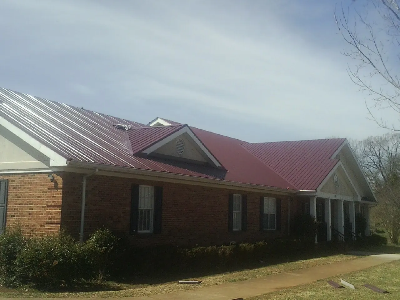 Red metal roof with gabled entries on a long brick building, from a Hail Damage Roof Repair job in Hughson