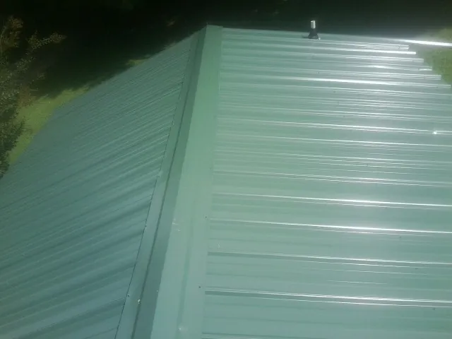 New green metal panels meeting at the ridge of a roof — Flat Roof Repair work by our crew in Hughson