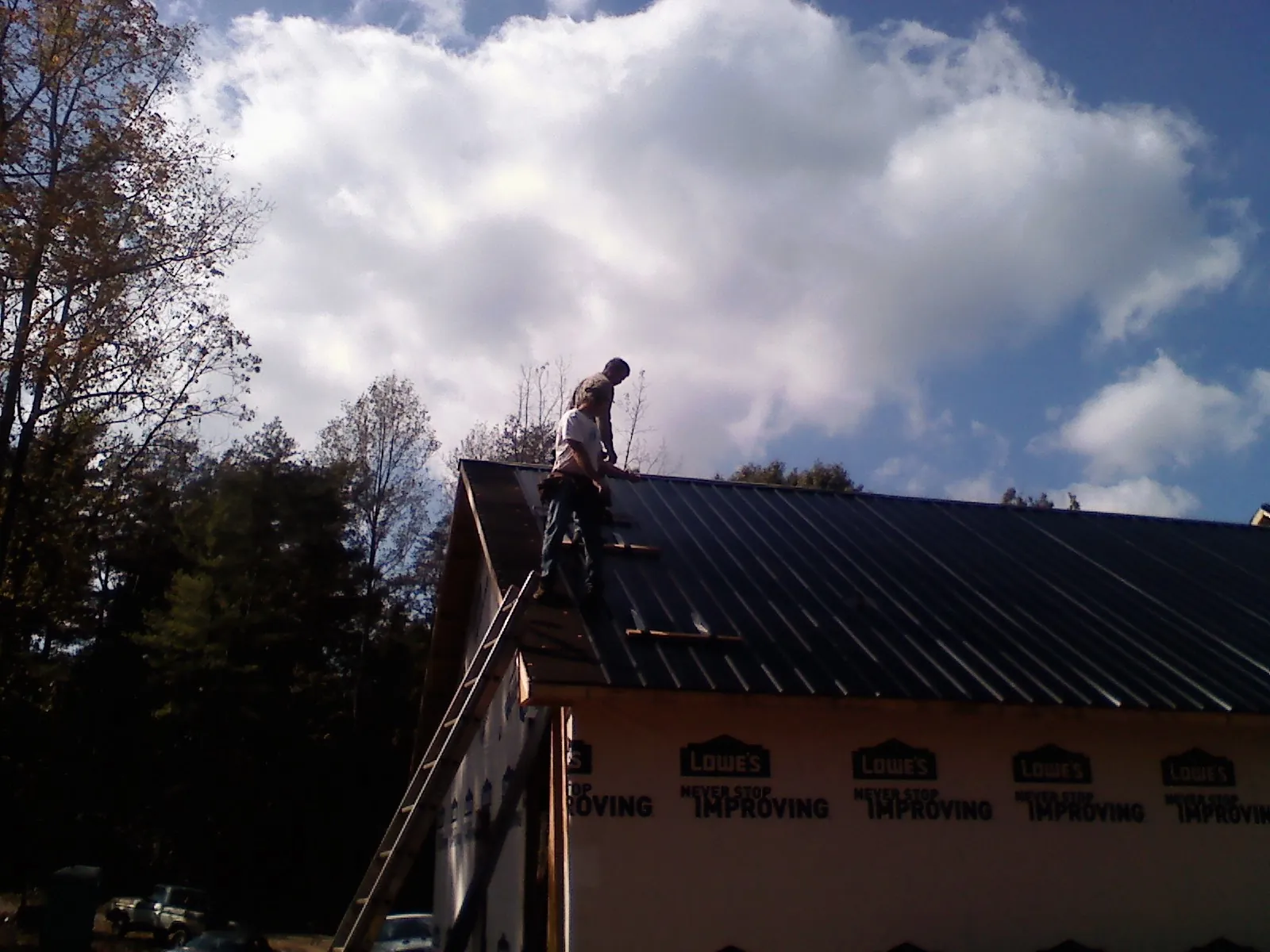Roofer fastening dark metal panels high against a cloudy sky, from a Roof Inspection job in Hughson