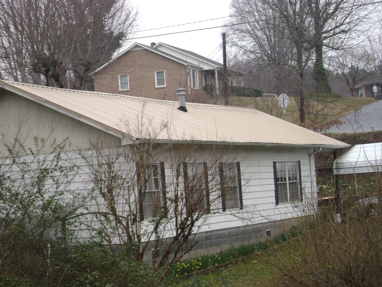 Tan metal roof on a white sided house set into a hillside — Commercial Roofing by Roofing Brothers in Hughson